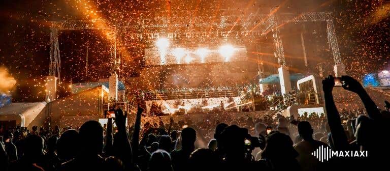 Groot outdoorfestival met confetti en krachtige podiumverlichting — juichende menigte bij een avondoptreden.