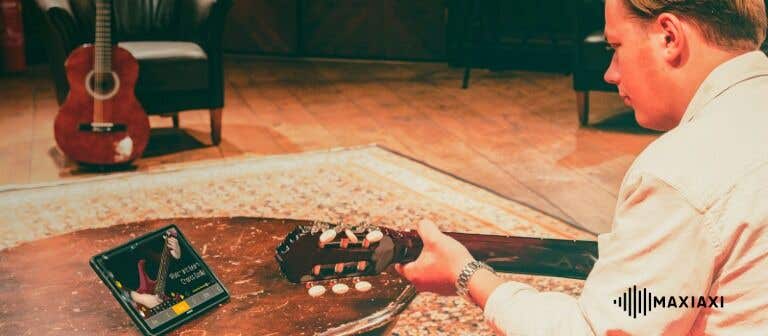 Mann übt Gitarre im Wohnzimmer mit Tablet – Gitarrenlernen mit Online-Unterricht und digitaler Unterstützung.