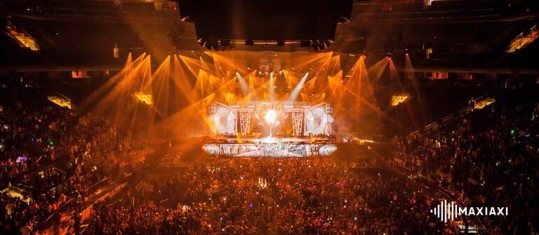 Ausverkaufte Konzerthalle mit orangefarbener Lichtshow – beeindruckende Bühnenbeleuchtung und feierndes Publikum.