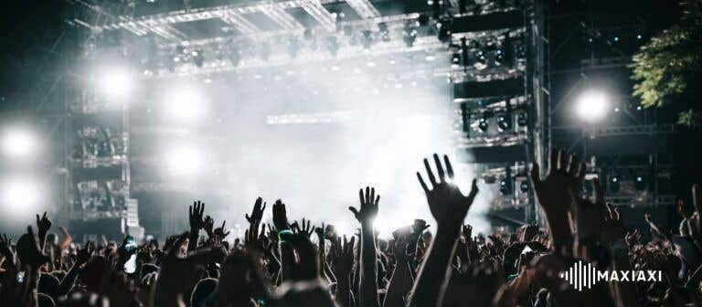 Großes Konzertpublikum mit erhobenen Händen vor einer hell beleuchteten Bühne – energiegeladene Stimmung bei einem Live-Konzert.