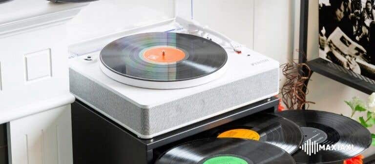 Weißer Plattenspieler mit aufgelegter Schallplatte auf einem Regal – Vinyl-Schallplatten ordentlich darunter gestapelt in einem Wohnraum.