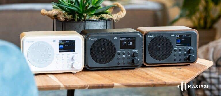 Drei Audizio DAB+-Radios in verschiedenen Farben auf einem Holztisch – moderne Digitalradios mit klarer Klangqualität und stilvollem Design
